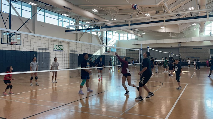 Youth playing volleyball on an indoor basketball court.