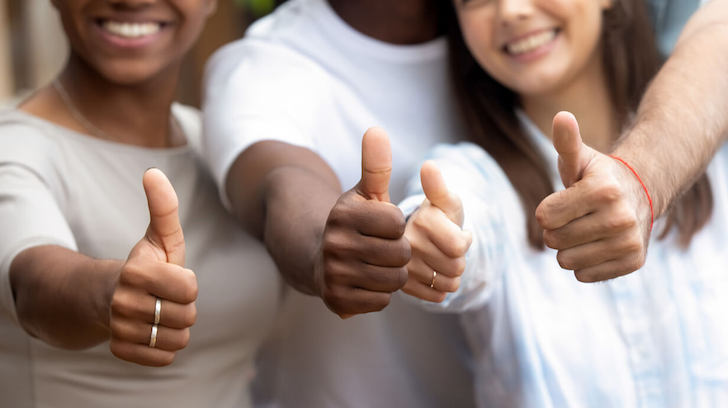 Four youth smiling and giving a thumbs up.